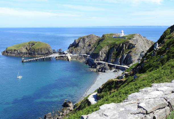 Looking down on the Landing Stage from the path up to the top of Lundy island The South lighthouse is on a large rock on the right and there is a white yacht moored in the harbour in the clear blue sea estuary stock pictures, royalty-free photos & images