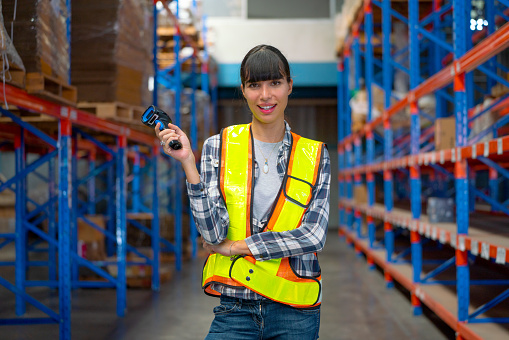 Portrait of Cacuasian warehouse worker hold barcode scaner and smile also look at camera stay on way between shelves in workplace. Concept of professional factory worker support for delivery system.