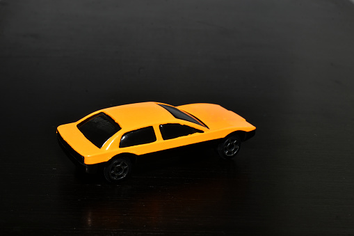 The picture shows a children's toy, a yellow car standing on a dark background.