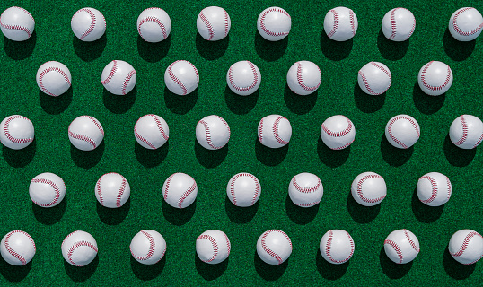 A high angle view looking down a rows of new baseballs on a green carpet outdoors.