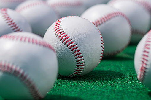 A low angle view with selective focus on one of the new baseballs that is in a row with others on a green carpet outdoors.