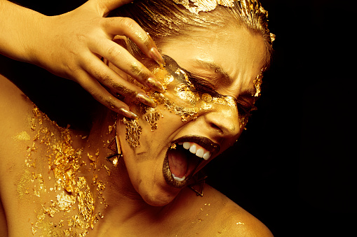 A beautiful girl rips off her face with golden makeup on a black background.