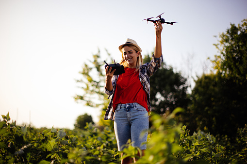 New generation of young woman with organic vegetable business, blonde girl on a raspberry field wearing casual clothing and hat, exploring the integrity of organic vegetables using drone