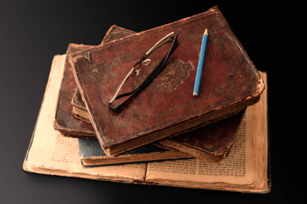 istock Stack of old worn jewish books in leather binding on open Torah pages on dark background. Closeup. Selective focus. 1409722310