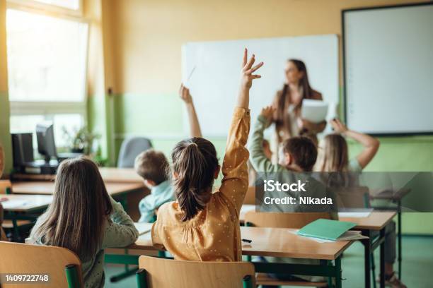 Schüler Die Die Hände Heben Während Der Lehrer Ihnen Im Klassenzimmer Fragen Stellt Stockfoto und mehr Bilder von Bildung