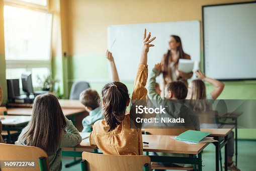 istock Students raising hands while teacher asking them questions in classroom 1409722748