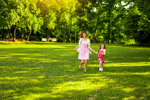 Playful young woman running with her little girl in the park on sunny spring day.