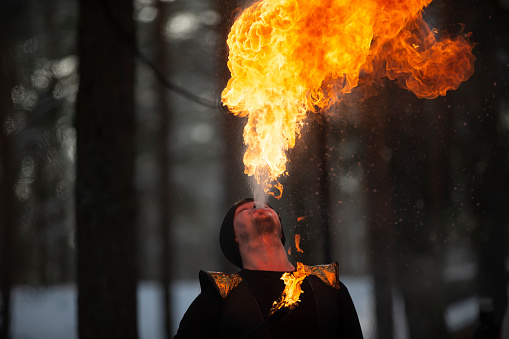 The man has fire and smoke coming out of his mouth. Fireshow.Young man blowing fire from his mouth