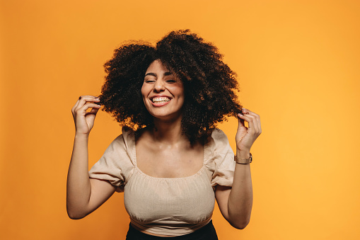 Young adult smiling woman against an orange yellow background is fixing her hair. Afro hair.
