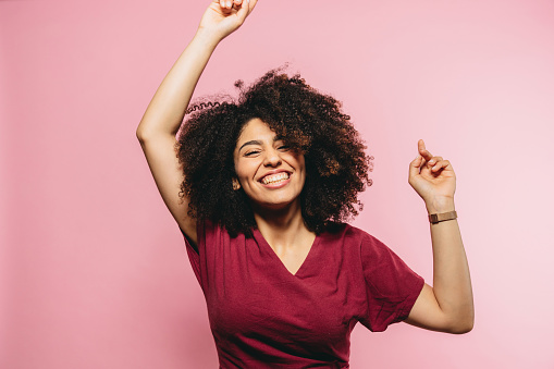 Young adult woman is dancing against a pink background. Happiness and freedom concept.