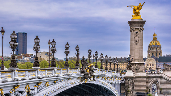 The ornate lanterns and statues of the Pont Alexandre III in Paris with the golden dome of the Invalides in the background.