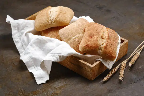 Italian ciabatta bread or bun in a wooden box with white kitchen napkin with spikelets of rye. Freshly baked traditional bread. Shallow depth of field