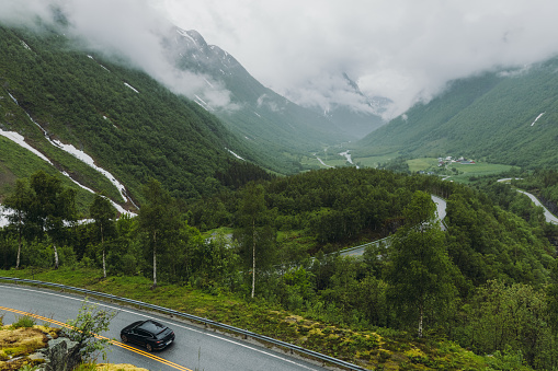 View off the car driving the road with view of the fresh green mountains during cloudy rainy summer day in Western Norway