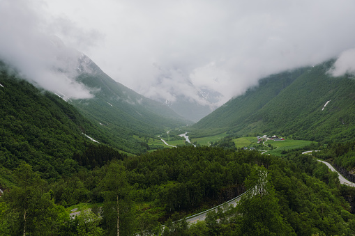 View off the car driving the road with view of the fresh green mountains during cloudy rainy summer day in Western Norway