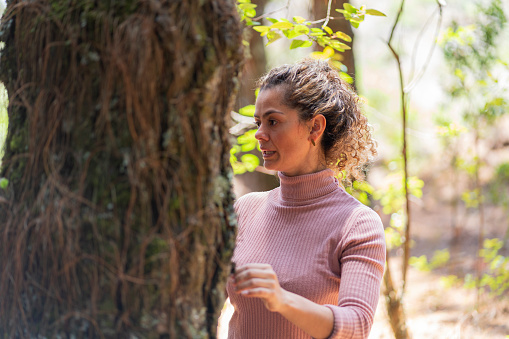 Latin woman of average age of 30 years is in a beautiful hotel in the middle of nature enjoying the trees and natural beauty with her eyes closed she hugs the trunk of a tree as a ritual of gratitude with nature