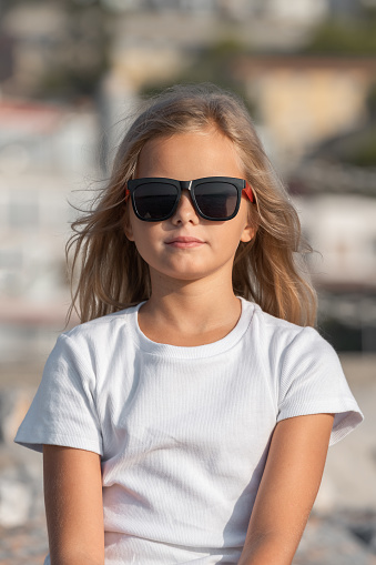 Portrait of a cute young girl with blond hair in sunglasses and a white t-shirt.