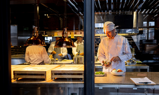 Latin American chef preparing food at the restaurant with his team of cooks - commercial kitchen concepts