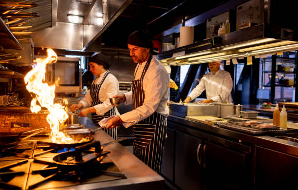 koch, der in einem restaurant kocht und das essen anzündet - gewerbliche küche stock-fotos und bilder