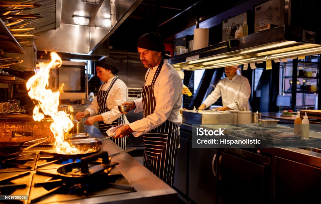 Chef cooking at a restaurant and flaming the food Latin American chef cooking at a restaurant and flaming the food on a pan - food and drink concepts Chef Stock Photo