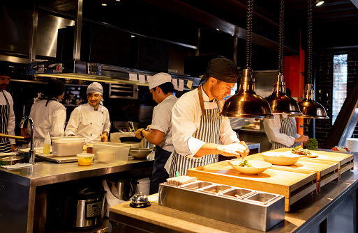 Young professional cook in uniform wiping kitchen counter in kitchen after cooking