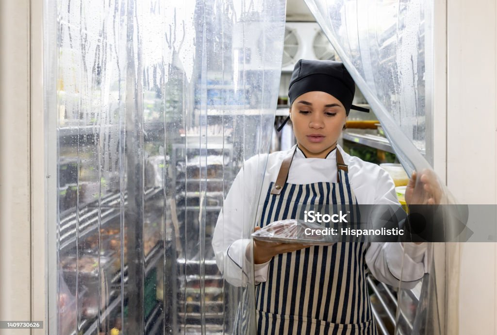 Chef working at a restaurant and grabbing some ingredients from the fridge Latin American chef working at a restaurant and grabbing some ingredients from the fridge - commercial kitchen concepts Refrigerator Stock Photo
