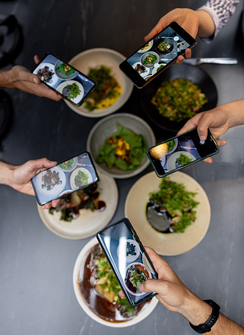 Close-up on a group of people eating at a restaurant and taking pictures of their food using their cell phones â social media concepts