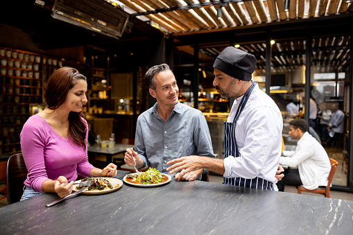Latin American chef talking to a couple eating together at a restaurant - food and drink service concepts