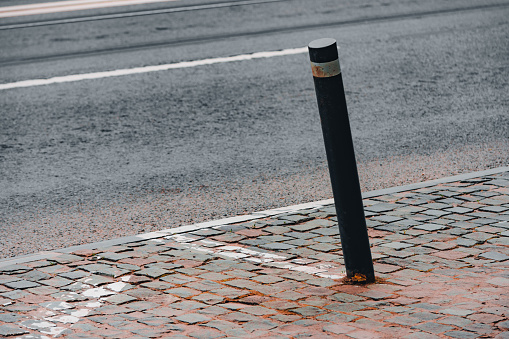 Bent black and white road pole bollard on a paved sidewalk