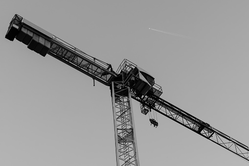 A crane from a lower view and an aircraft in the sky