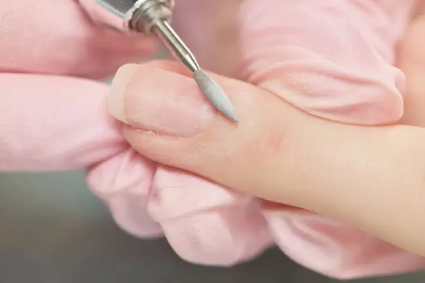 Manicurist filing client's nails at table, close up. Removing the nail plate with a milling machine. Selective focus