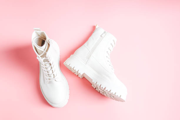 White demi-season boots made of eco-leather with fasteners, laces and rough soles on a pink. White demi-season boots made of eco-leather with fasteners, laces and rough soles lie on a pink background, flat lay close-up. The concept of fashion and women's shoes. lace fastener photos stock pictures, royalty-free photos & images