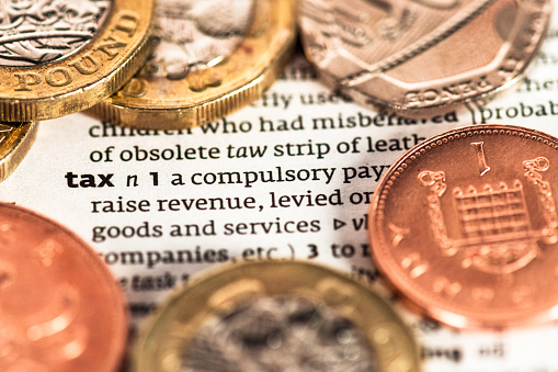 A close-up on a dictionary definition of the word 'tax', surrounded by UK coins.