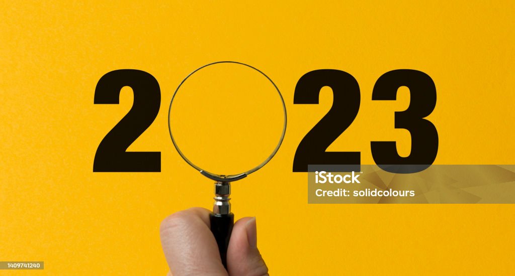 2023 typed on yellow background. O letter replacement with magnifying glass. A hand holding the magnify. 2023 Stock Photo