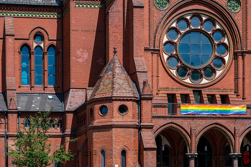 Detail shot of the entrance area and the facade of the Heilig-Kreuz-Church in Berlin Kreuzberg. A rainbow flag hangs over the entrance.