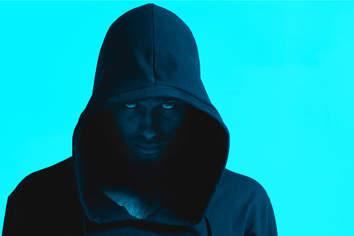 Male portrait of black African-American man at the studio in neon lighting. Color background, copy space for template. Serious handsome person wear dark hoodie is posing for camera