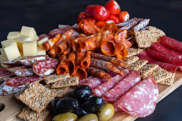 Cutting board with prosciutto, salami, cheese,bread sticks and olives. Cutting board with ham, salami, cheese, crackers and olives on a dark stone background. salumeria stock pictures, royalty-free photos & images