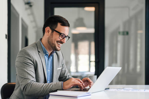 istock Smiling young man working on laptop in modern office, checking email in the morning. 1409751243