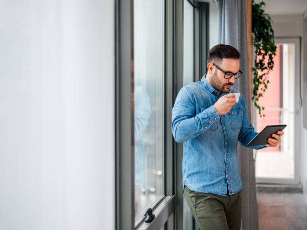istock Young businessman or entrepreneur using digital tablet while enjoying coffee by the window at business office 1409751246