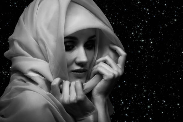beautiful young woman with white headscarf cover her face with luxury makeup on stars background looking down, monochrome