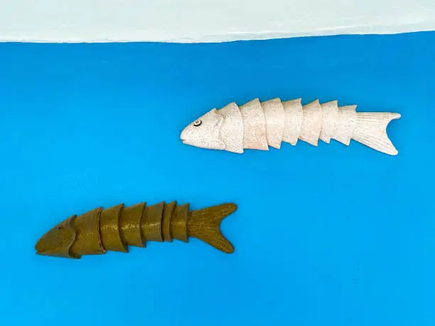 Photo of sea fish made of metal and iron. application, white and brown rubber fish. bait for fishing, fish on a blue matte background