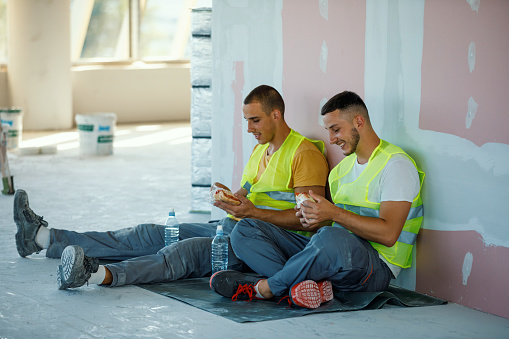 Two Caucasian male construction workers are having a cheerful conversation while taking a lunch break.