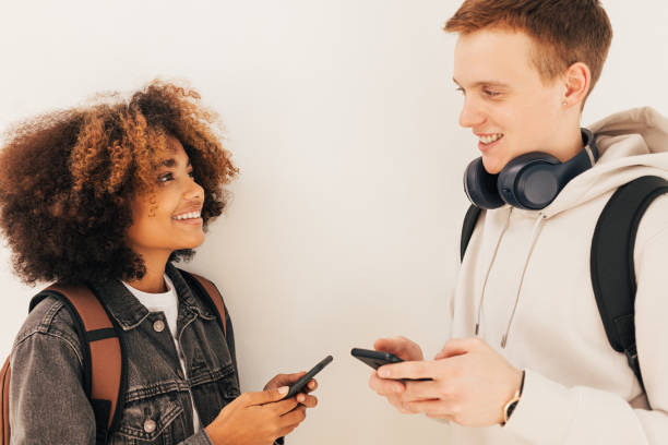 istock Two classmates standing at wall and looking to each other holding smartphones 1409758891