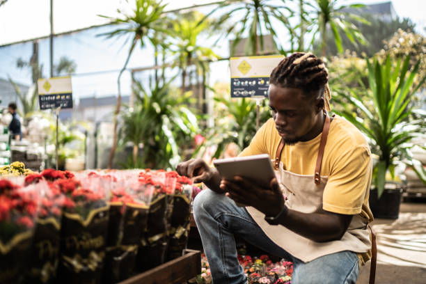 jovem vendedor trabalhando em um tablet digital em um centro de jardim - florist flower market flower store - fotografias e filmes do acervo