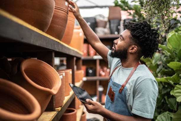 joven vendedor trabajando en una tableta digital en un centro de jardinería - florist fotografías e imágenes de stock