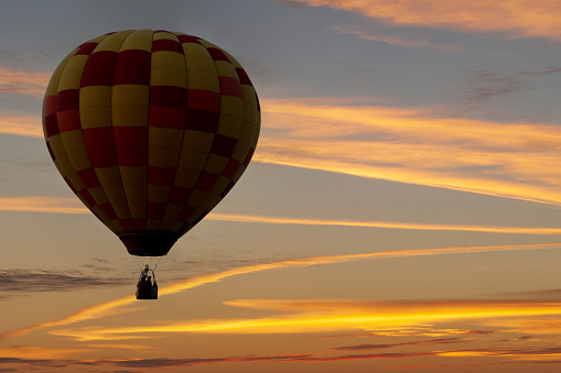 A hot air balloon floats against a sky painted yellow and orange by the setting sun in a composite image.