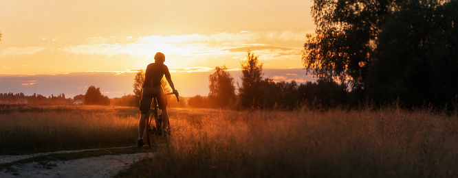 Silhouette of Cyclist rides countryside dirt road at sunset. Panoramic view. Sport concept.