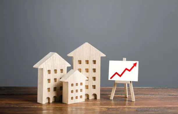 Photo of Residential buildings and easel with a positive growth trend red arrow up chart. Market growth, attracting investment. Raising taxes and house maintenance. Real estate price increases. High value
