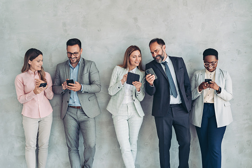 Group of business people standing against a concrete wall and using mobile devices