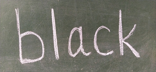 The word BLACK written by hand on a green school board. Black color. Printed letters.