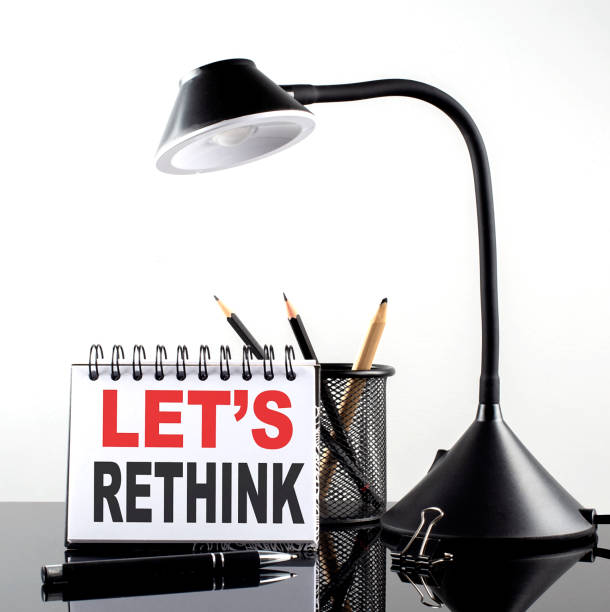 LET S RETHINK text on notebook with pen and table lamp on the black background stock photo